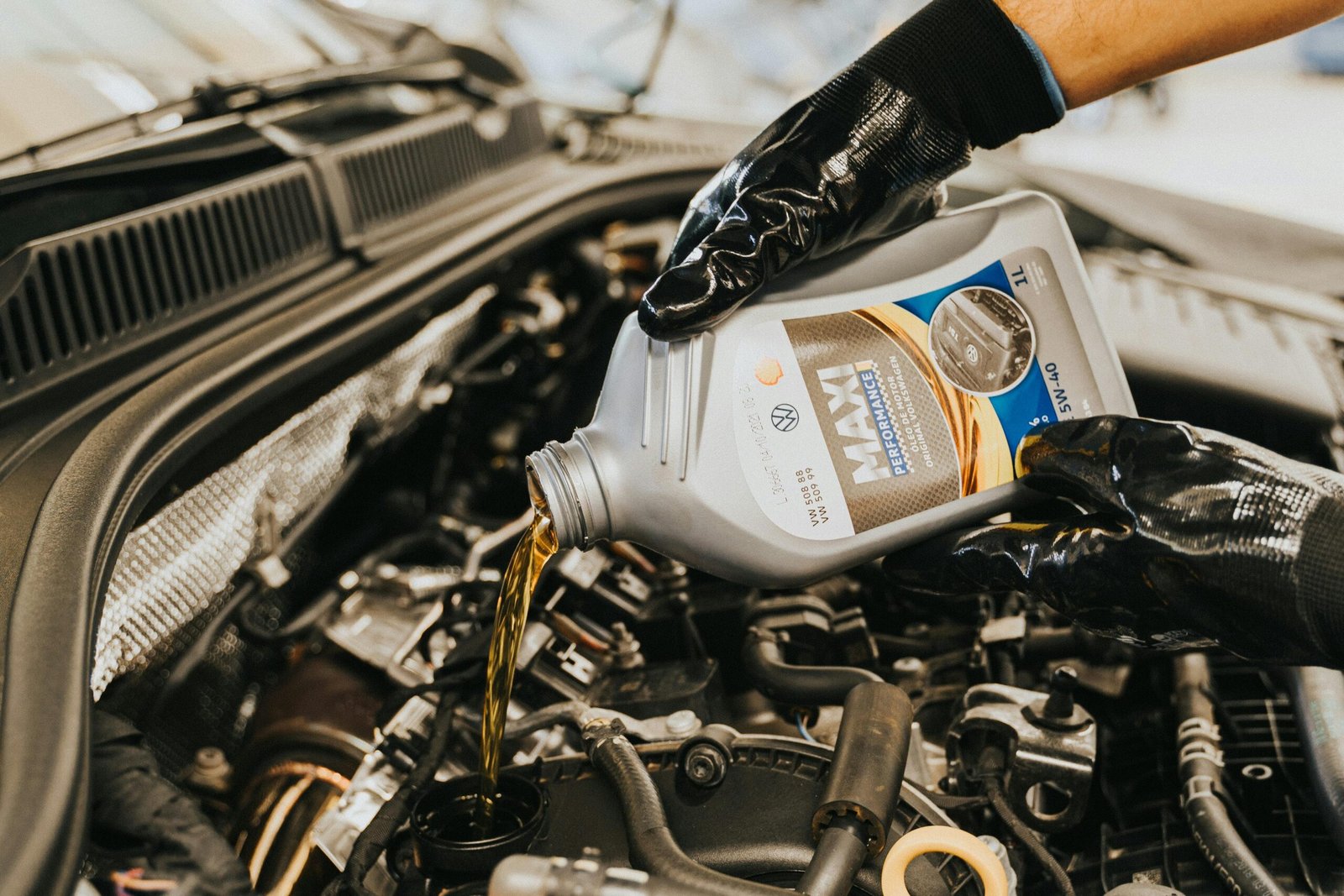 A mechanic wearing gloves pouring oil into a car engine in a garage setting.
