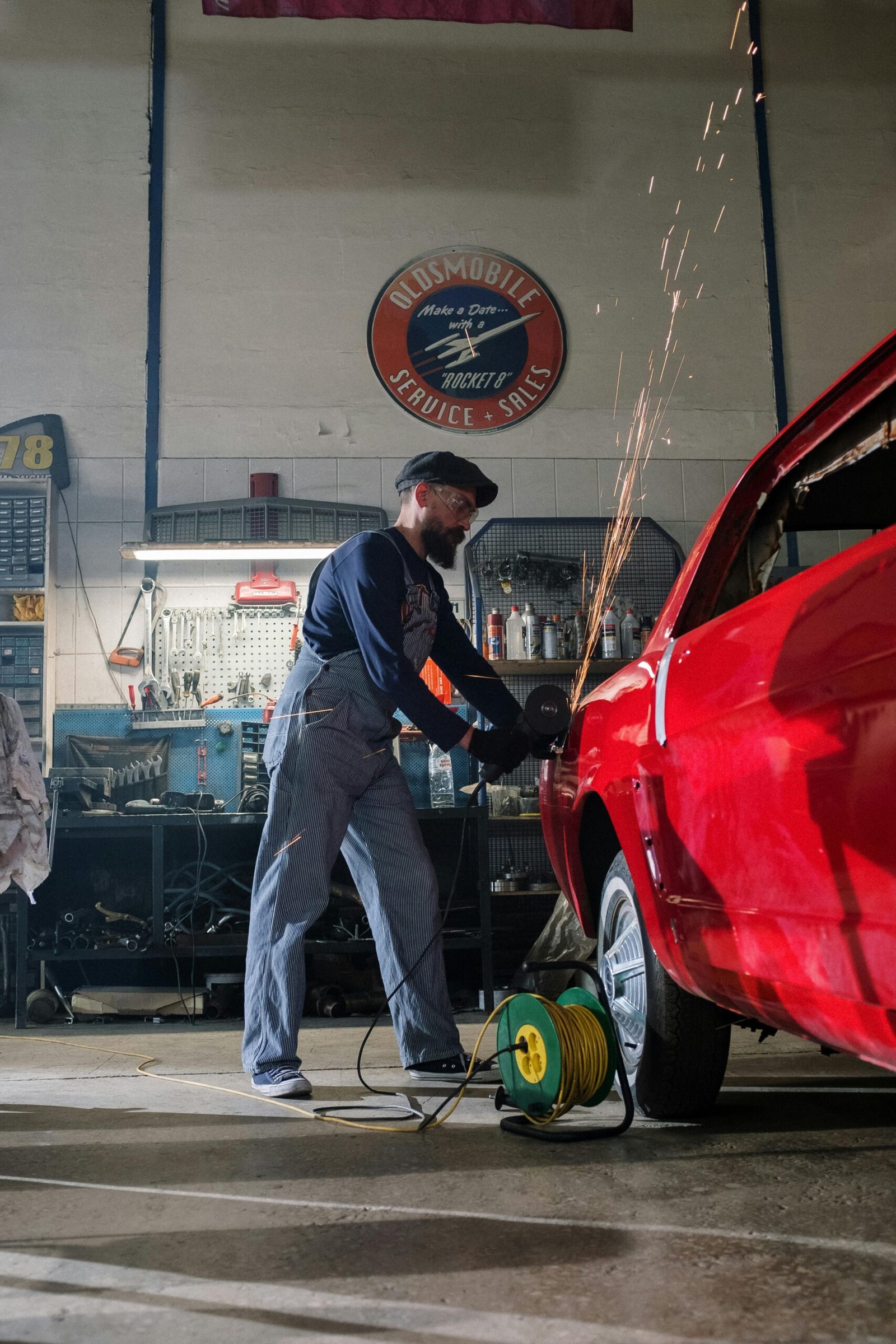 Mechanic using grinder on car body in a busy garage, sparks flying as he works.