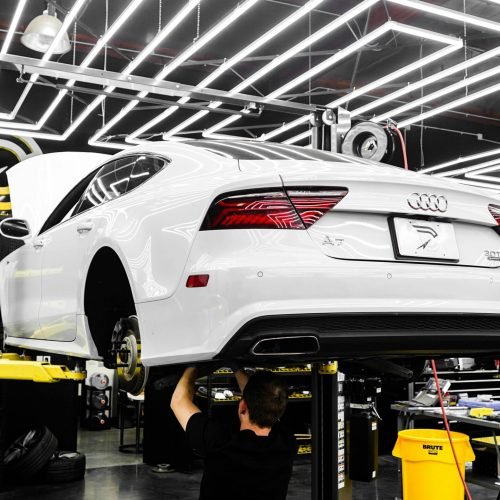 White luxury car being serviced by mechanic in a modern garage setting.
