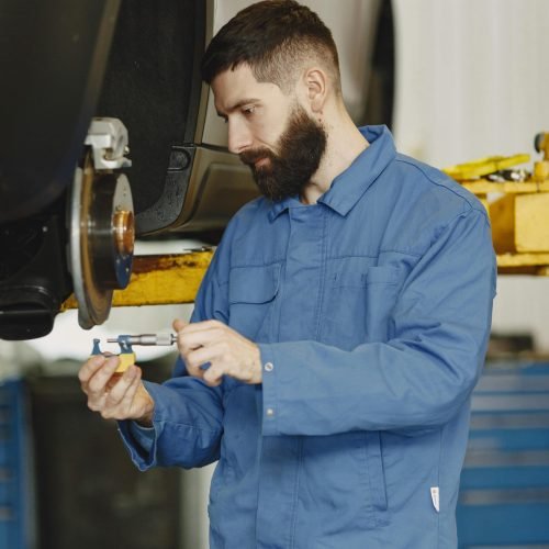 Mechanic in blue uniform inspecting car brakes in garage setting.